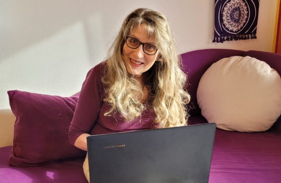 Christine sitzt am Sofa und LapTop auf dem Schoß